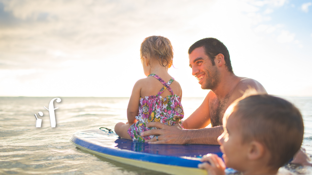 two kids playing in the ocean with their father